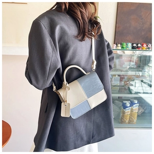 Detail of color-block crossbody bag on a gray blazer, featuring a chic top handle and tag