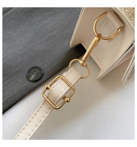 Close-up of golden metal buckle and silver rhinestones on a cream shoulder bag