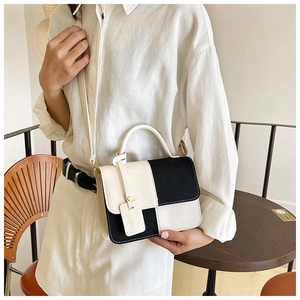 Detail of color-block leather shoulder bag with golden brand tag worn by a model