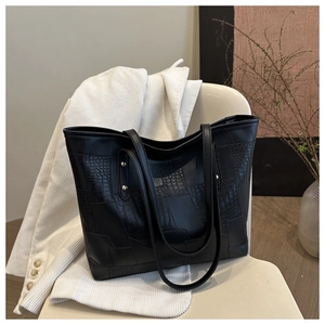 Detail of crocodile embossed leather tote bag with gold rivets on a white chair