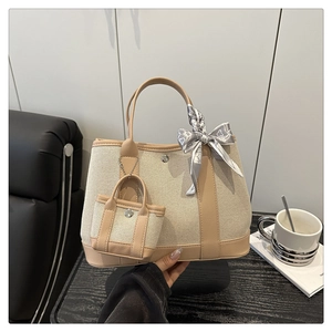 Detail of beige canvas tote with faux leather trim, mini charm, and patterned silk scarf