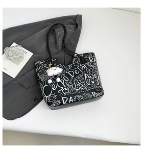 Dettaglio della borsa tote in pelle nera con illustrazioni graffiti bianche e ciondolo a nuvola