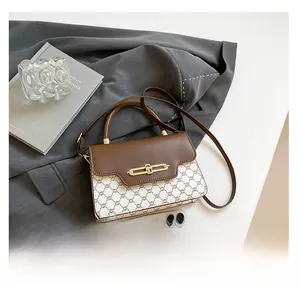 Detail view of small crossbody bag with vintage print and gold lock next to a phone