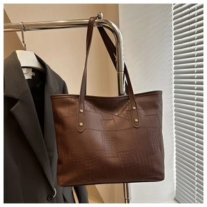Detail of dark brown tote bag with crocodile texture stitching and gold stud hardware