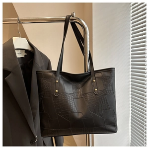 Detail of black tote bag showing crocodile and lizard texture with golden metal rivets