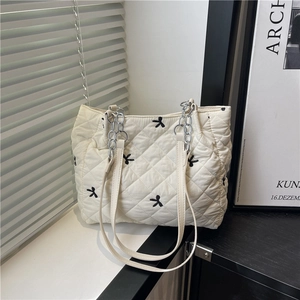 White quilted tote bag with black bow embroidery and silver chain handles in minimalist style