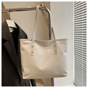 Close-up of white tote bag featuring crocodile pattern texture and gold metal studs