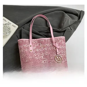 Détail du cabas rose à damier avec pendentif M doré et fines bretelles de transport