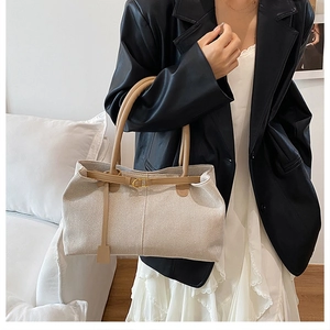Detail of canvas tote bag with leather trim and gold buckle shown on a model