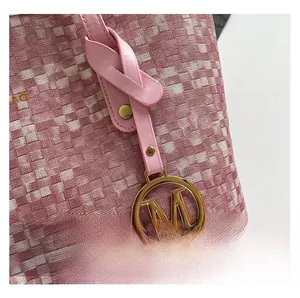 Détail du sac cabas rose tissé avec pendentif logo M doré et finitions cloutées chic