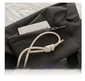 Close-up of white leather handbag featuring a knotted cylindrical handle and gold metal end