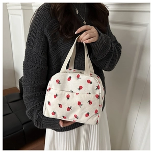 Detail of corduroy tote bag with strawberry print held by model in casual outfit
