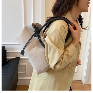 Chic off-white canvas tote bag with black leather straps worn by a model in a minimalist room
