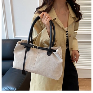 Detail of beige canvas tote bag with black leather straps and gold metal hardware accents