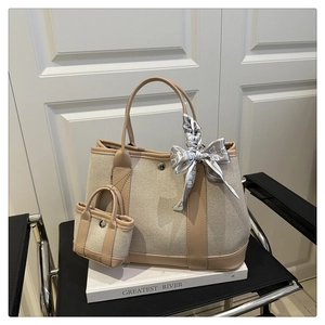 Detail of beige canvas tote with brown leather trim, silk scarf, and mini charm bag