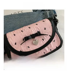 Détail du sac bandoulière rose à volants avec nœud en cuir et pendentif cœur en métal