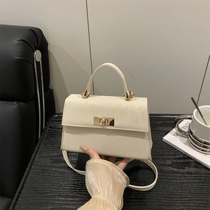 Minimalistische cremeweiße Trapez-Handtasche mit Goldschnalle und Gurt auf dunklem Holztisch