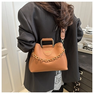Dettaglio borsa a mano in pelle marrone con manico in metallo traforato e catena decorativa