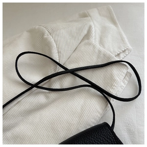 Close-up of black lychee grain leather mini bag with thin shoulder strap on white fabric