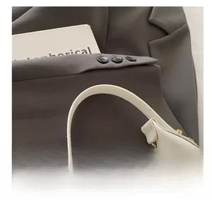 Detail of white leather crescent bag with gold zipper and stud hardware on a grey blazer