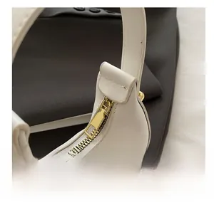 Close-up of white crescent handbag featuring a smooth golden zipper and refined stitching