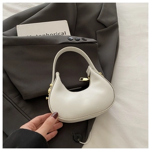 Close-up of a white crescent handbag with gold zipper on a gray blazer and prop book