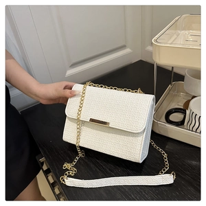 Detail of woven texture faux leather on white crossbody bag with gold chain strap