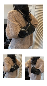 Detail of glossy black patent leather hobo bag with silver metallic buckle on a knit sweater
