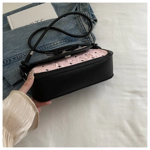 Détail du nœud rose et motif monogramme sur sac à bandoulière noir en cuir