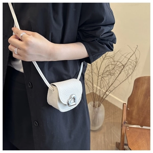 Détail du mini sac selle blanc avec boucle en forme de cœur et texture grainée