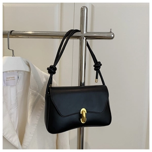 Detail of black leather handbag featuring a gold oval magnetic lock and knotted strap