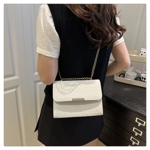 Detail of white woven textured handbag with gold chain strap shown on a model