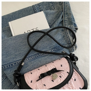 Détail du sac à main rose gaufré avec nœud noir, charm cœur et motifs de lapins