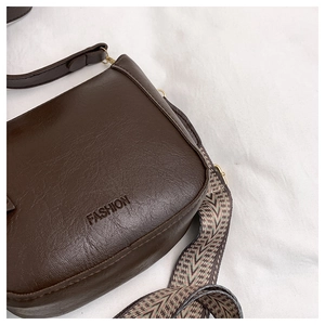 Close-up of brown textured leather bag with FASHION logo and colorful woven strap