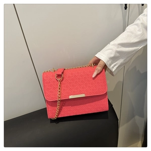 Detail of coral pink crossbody bag with woven texture and gold chain strap