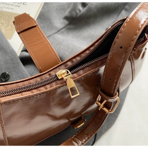 Gros plan d'un sac en cuir verni marron montrant le zip doré et les coutures fines