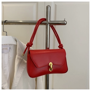 Detail of red faux leather shoulder bag with gold oval lock and knotted strap design