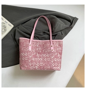 Detail view of pink woven tote bag showing leather handles and gold rivet hardware
