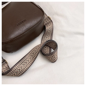 Detail of dark brown bucket bag with lychee texture and wide woven geometric strap