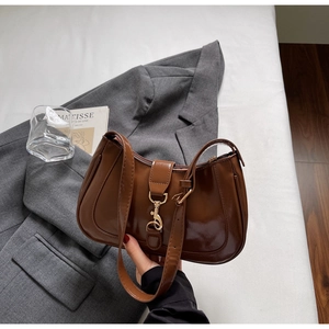 Détail du sac en cuir verni marron avec boucle dorée posé sur un blazer gris chic