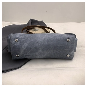 Detail of blue denim tote bag bottom with protective silver metal studs and brown strap
