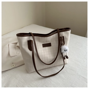 Detail of cream houndstooth tote bag with brown leather trim and plush charm