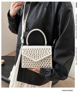 Detail of white leather crossbody bag with V-shape design and silver rivet studs on model