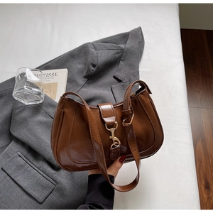 Detail view of a brown glossy baguette bag with a golden piston clasp on a grey blazer
