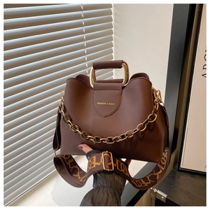 Dettaglio borsa marrone con catena dorata e ampia tracolla con motivi decorativi chic