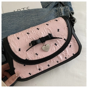 Détail du sac à main plissé rose avec motifs nœuds noirs et breloque cœur en métal
