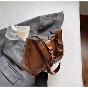 Détail d'un sac demi-lune en cuir ciré marron avec boucle dorée sur un costume