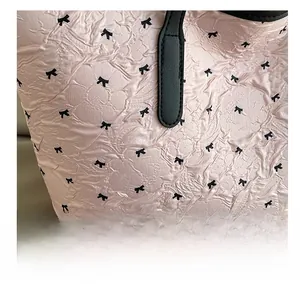 Close-up of pink pleated fabric with black bow patterns and leather handle on a tote bag
