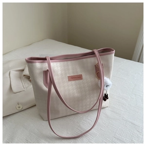 Detail of beige houndstooth tote bag with pink leather handles and plush charm