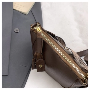 Detail of dark brown leather bucket bag showing zipper texture and woven shoulder strap